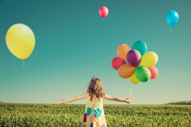 a girl in a dress holding a bunch of balloons.